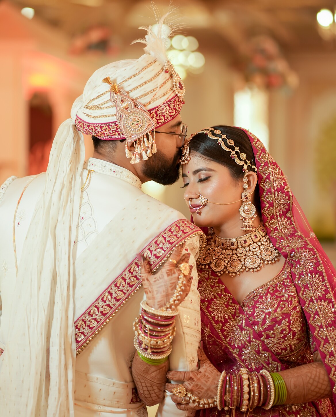 Bride holding her husband's arm as he kisses her forehead at a Jaipur wedding